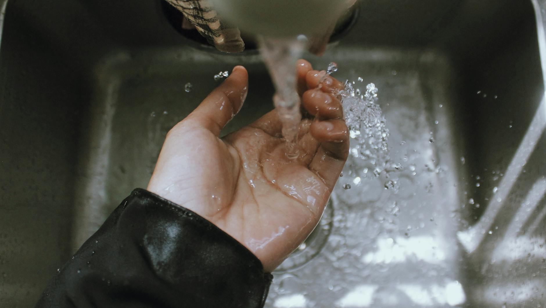 Close-up of a hand being washed under a stream of running water in a sink, emphasizing cleanliness.